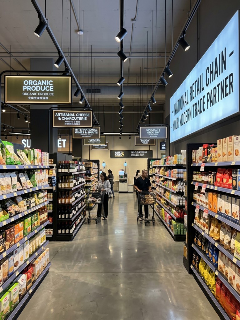 Magazin alimentar modern premium, culoar larg, semnalistică categorii și clienți cu coșuri — modern trade